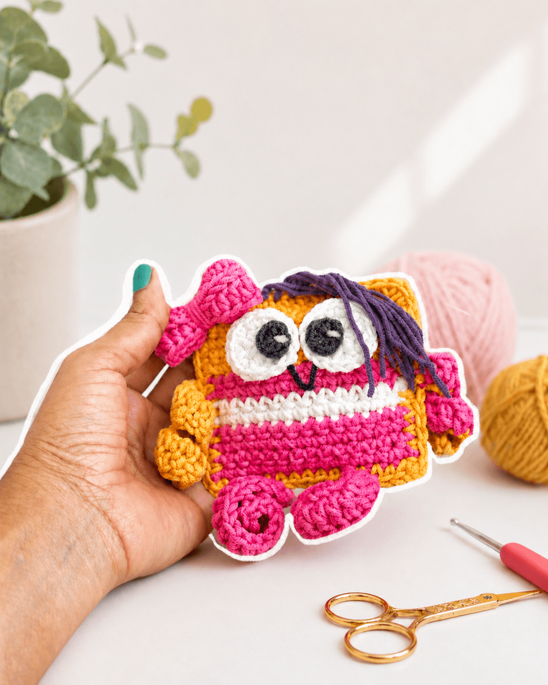 A colorful handmade crochet owl held beside yarn and crochet tools
