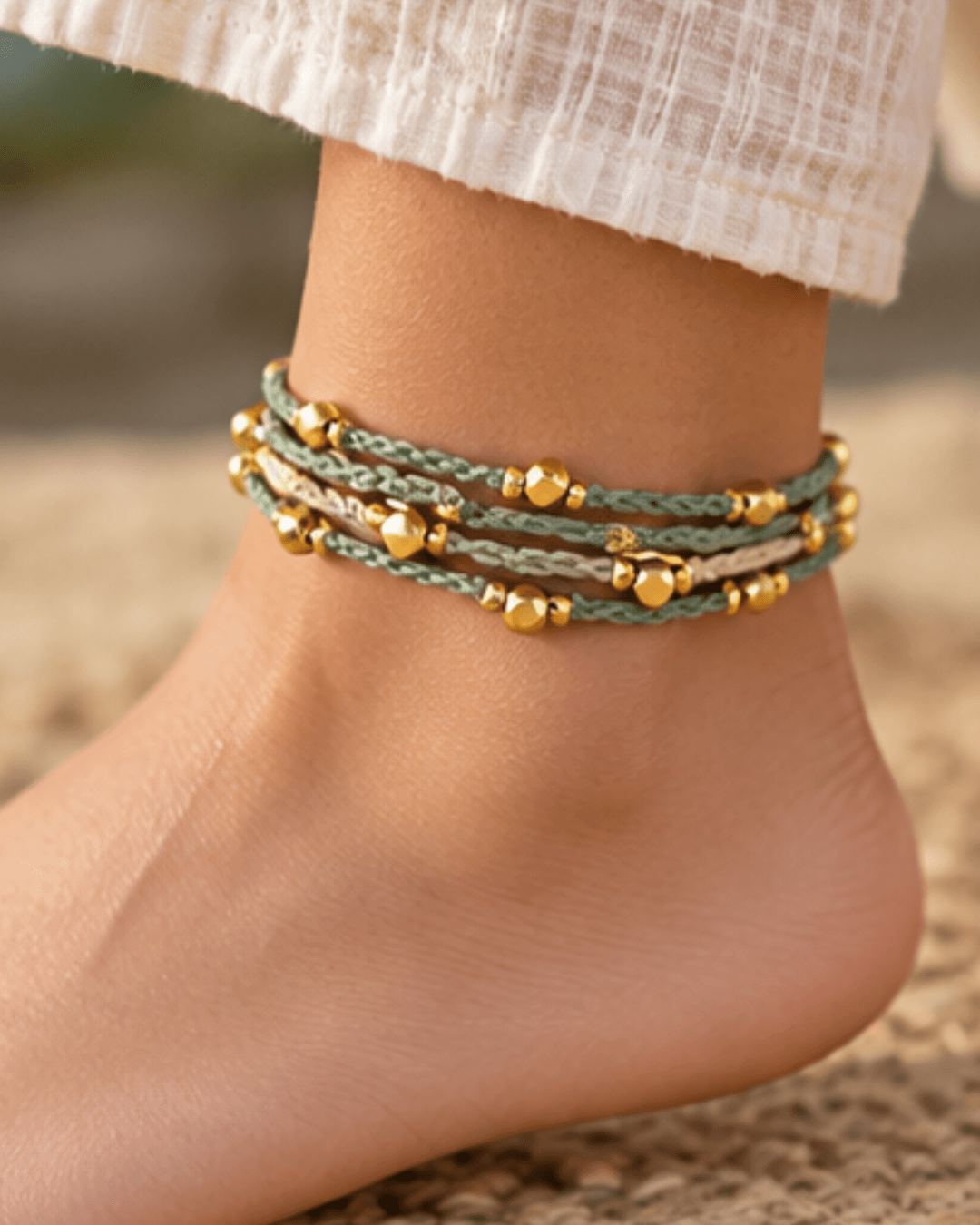 A green crochet wrap anklet with gold beads, worn around an ankle
